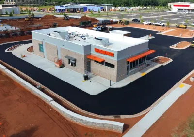 Whataburger fast-food restaurant under construction with orange awnings, brick facade, and a surrounding black paved drive-through loop; construction equipment and dirt piles visible in the background.